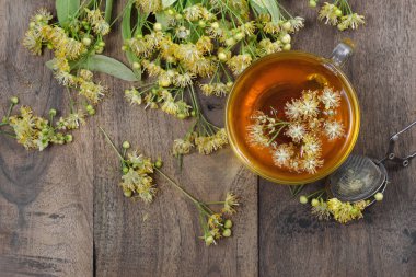 Tahta bir masada bir fincan ıhlamur çayı ve taze ıhlamur çiçeği. Bitki çayı. en üstteki görünüm