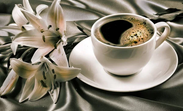 coffee in a white cup. cup of coffee and white lily flower on a silk background. romantic coffee. black and white
