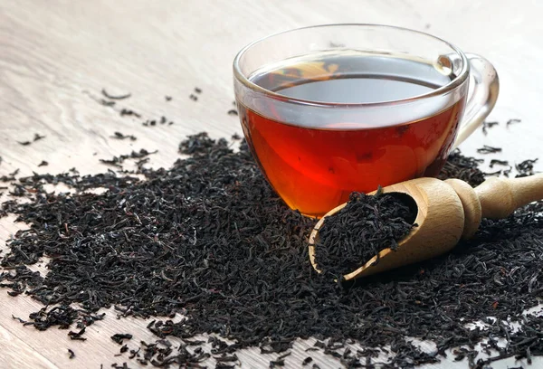 concept i like tea. a cup of black tea and dry black tea leaves on a wooden table. heart symbol made from black tea leaves