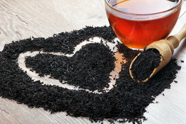 concept i like tea. a cup of black tea and dry black tea leaves on a wooden table. heart symbol made from black tea leaves