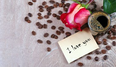 Not: Seni seviyorum. Bir fincan kahve, kavrulmuş kahve çekirdekleri ve ahşap bir masada kırmızı gül. Romantik kahve. Üst Manzara. Boşluğu kopyala