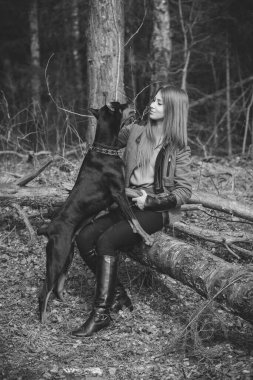 Genç kız ormanda doberman köpeğiyle oynuyor.