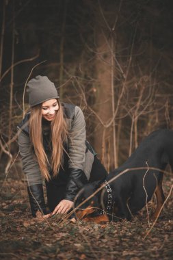 Genç kız ormanda doberman köpeğiyle oynuyor.