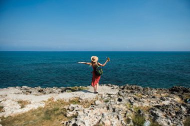 Sırt çantalı ve pina colada 'lı genç bir kadın denize bakıyor.