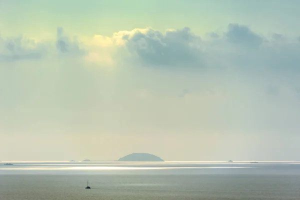 CALM SEA ON A HAZY DAY. Scenic view of calm sea on a hazy day with a yacht and islands in a distance.