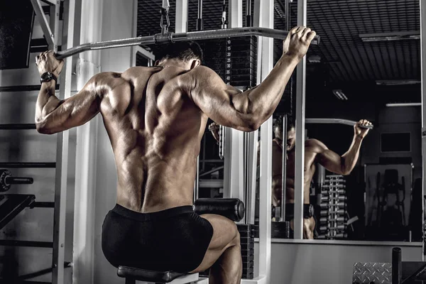 ボディービルダーの人 暗い体育館で 背中の広い筋肉運動マシンで運動を行う — ストック写真