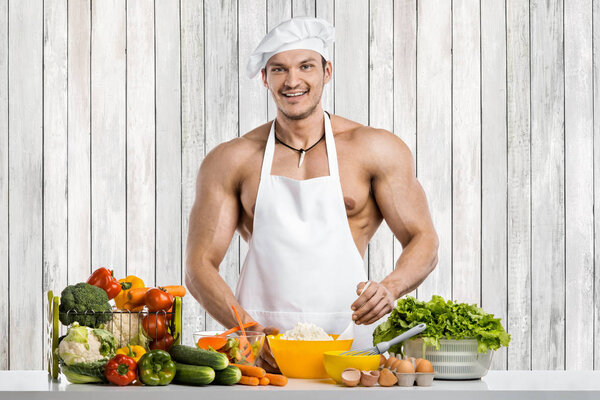 Человек культурист на кухне в белом токе одеяло и готовить защитный фартук приготовления творога и овощей
