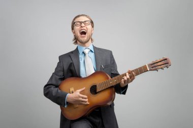 Gri arkaplanda gitar çalan ve yüksek sesle şarkı söyleyen bir işadamı ya da ofis çalışanı portresi