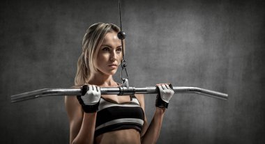 Güzel fitness kadını egzersiz yaparken gri duvar arka planında egzersiz makinası kullanıyor. 