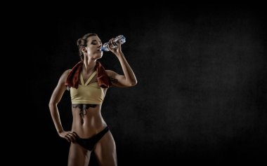 Genç fitness kadını siyah zemin üzerinde şişe suyu içiyor ve mesaj için boş bir alan var.