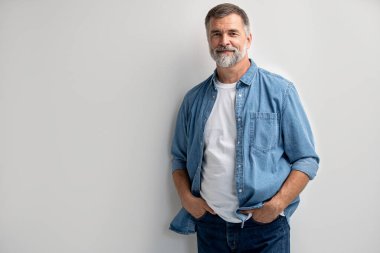 Beyaz arka planda duran gülümseyen olgun bir adamın portresi.