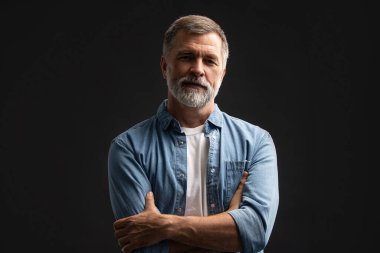 Siyah arka planda duran gülümseyen olgun bir adamın portresi.