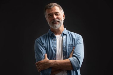 Siyah arka planda duran gülümseyen olgun bir adamın portresi.