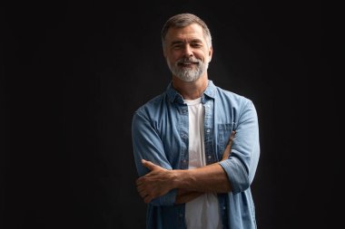 Siyah arka planda duran gülümseyen olgun bir adamın portresi.