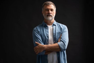 Siyah arka planda duran gülümseyen olgun bir adamın portresi.