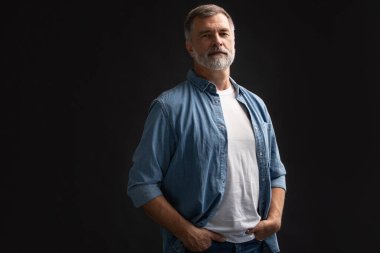 Siyah arka planda duran gülümseyen olgun bir adamın portresi.