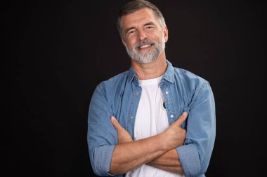 Siyah arka planda duran gülümseyen olgun bir adamın portresi.
