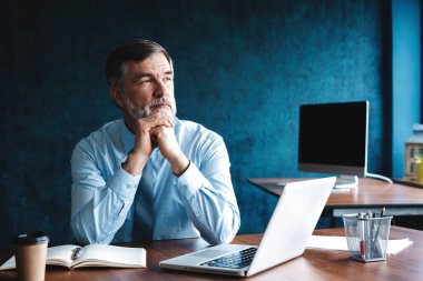 Modern ofiste bir masada otururken düşünce derin odaklanmış olgun işadamı.