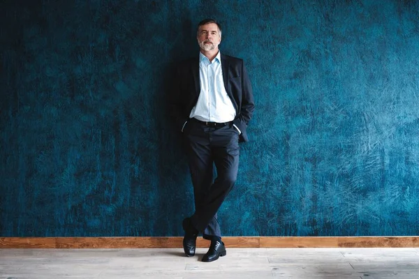 Serieuze volwassen man poseren in de voorkant van een donkerblauwe achtergrond met kopieerruimte. — Stockfoto