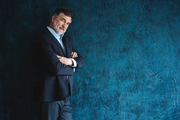 Serieuze volwassen man poseren in de voorkant van een donkerblauwe achtergrond met kopieerruimte. — Stockfoto