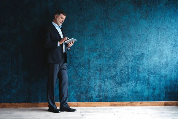 Ευτυχισμένος ώριμος επιχειρηματίας που εργάζεται με σύγχρονη ταμπλέτα απομονώνονται σε σκούρο μπλε φόντο. — Φωτογραφία Αρχείου