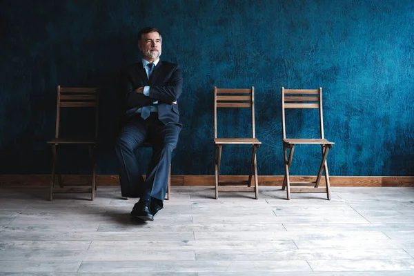 Esperando la entrevista. Confiado hombre de negocios maduro sentado en la silla sobre fondo azul oscuro . —  Fotos de Stock