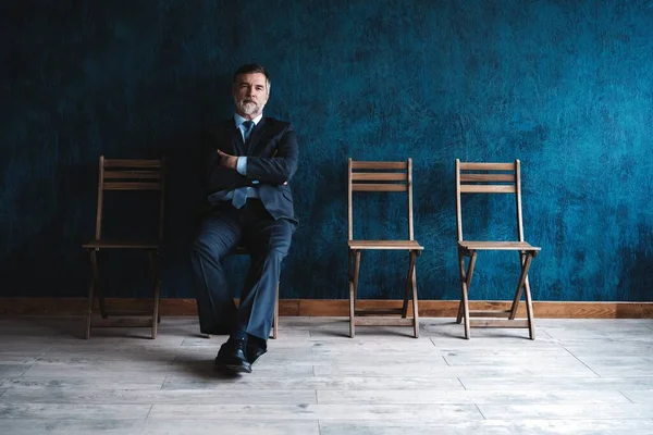 Esperando la entrevista. Confiado hombre de negocios maduro sentado en la silla sobre fondo azul oscuro . —  Fotos de Stock