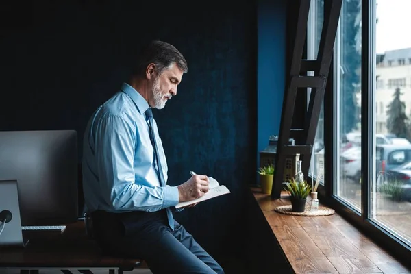Concentrado en el trabajo. Enfocado hombre de negocios maduro trabajando y tomando notas en su oficina moderna . — Foto de Stock