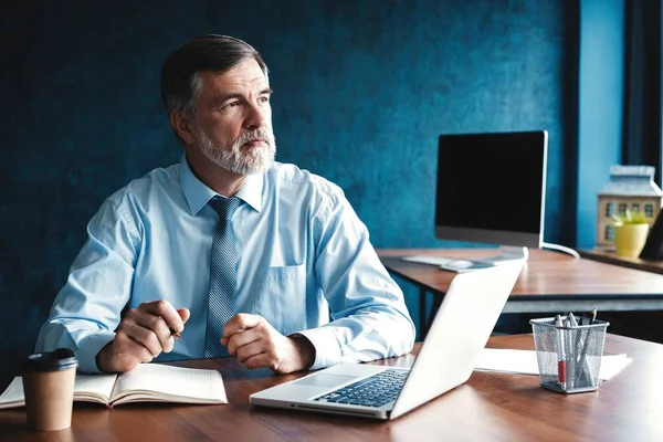 Gerichte volwassen zakenman diep in gedachte terwijl zittend aan een tafel in modern kantoor. — Stockfoto