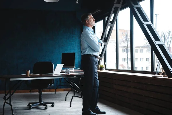Volwassen zakenman in een corporate Suit staande in kantoor en kijk weg door grote ramen optimistisch. — Stockfoto