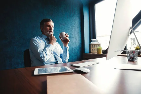 Gerichte volwassen zakenman diep in gedachte terwijl zittend aan een tafel in modern kantoor. — Stockfoto