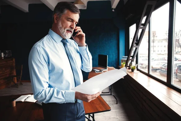 Contador concentrado enfocado, hombre de negocios maduro mirando el informe, se encuentra en traje completo, tan exitoso e inteligente, estación de trabajo moderna . —  Fotos de Stock