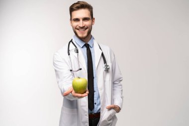 Beyaz önlüklü yakışıklı doktorun portresi kameraya bakıyor ve beyaz bir elmayı tutarken gülümsüyor..