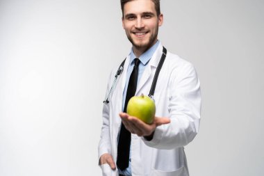Beyaz önlüklü yakışıklı doktorun portresi kameraya bakıyor ve beyaz bir elmayı tutarken gülümsüyor..