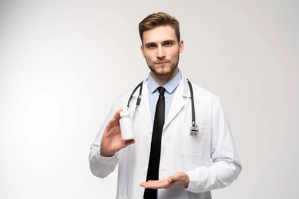 Glimlachende arts met een fles tabletten of pillen met een blanco wit etiket voor de behandeling van een ziekte of letsel. — Stockfoto