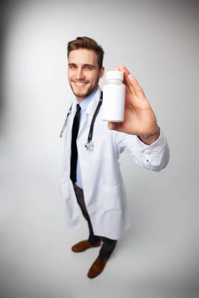 Χαμογελώντας γιατρός κρατώντας ένα μπουκάλι δισκία ή χάπια με λευκή ετικέτα για τη θεραπεία μιας ασθένειας ή τραυματισμού. — Φωτογραφία Αρχείου