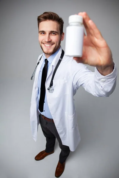 Glimlachende arts met een fles tabletten of pillen met een blanco wit etiket voor de behandeling van een ziekte of letsel. — Stockfoto