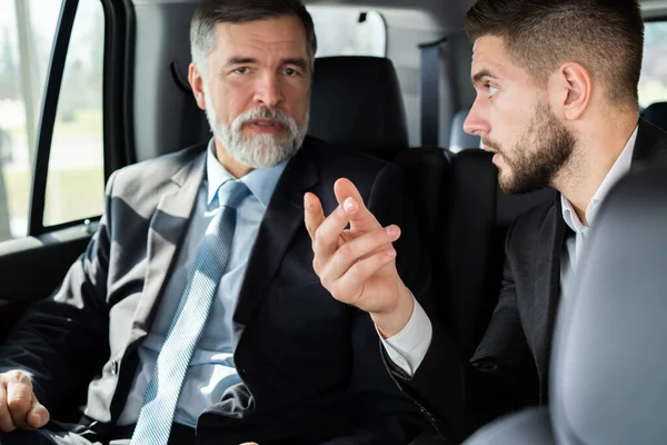 Affärskollegor diskuterar affärsidéer medan du sitter i baksätet på bilen eller taxin. — Stockfoto