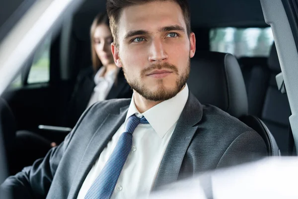 Succes in beweging. Knappe jongeman in vol pak glimlachend terwijl hij in een auto rijdt. — Stockfoto