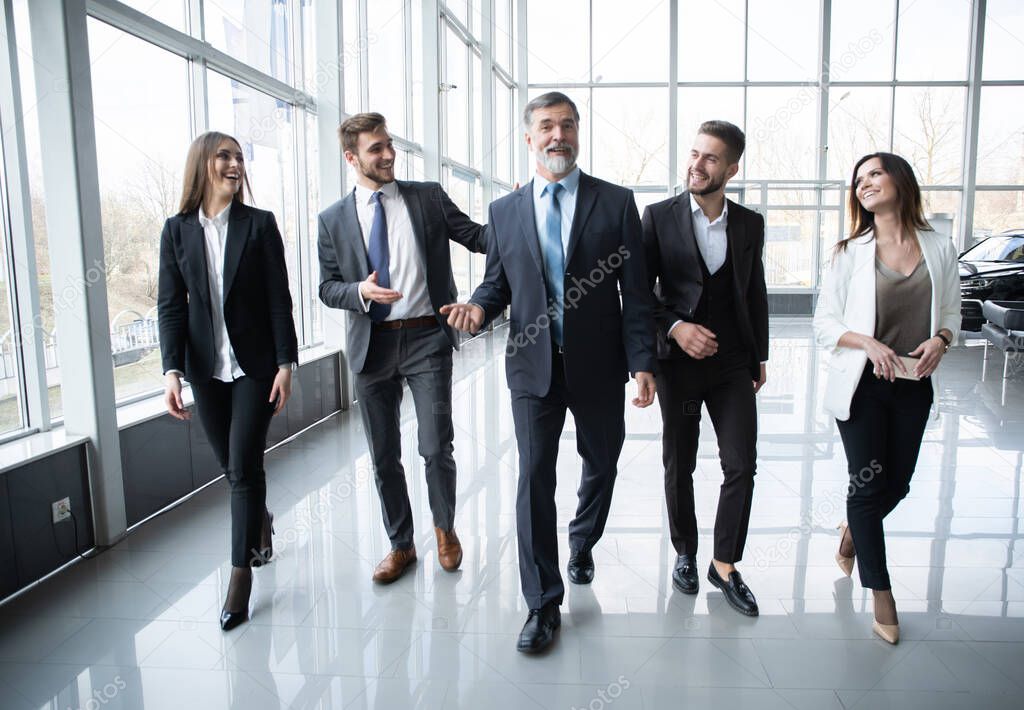 Business People Team Walking In Modern Office, Confident Businessmen And Businesswomen With Mature Leader In Foreground.