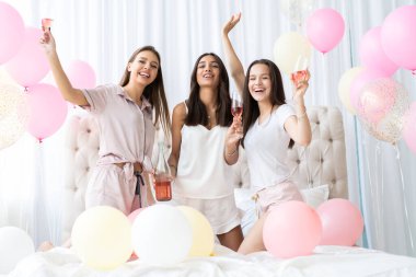 Pijama partisi. Çekici, pijamalı, gülümseyen kadınlar yatak odasında pijama partisi yaparken şampanya içiyorlar..