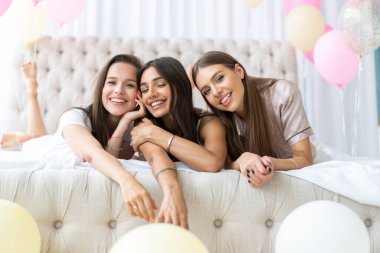 Pijama partisi. Çekici, pijamalı, gülümseyen kadınlar yatak odasında pijama partisi yaparken şampanya içiyorlar..