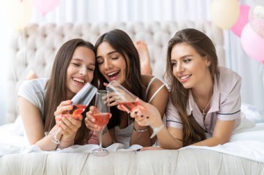 Pijama partisi. Çekici, pijamalı, gülümseyen kadınlar yatak odasında pijama partisi yaparken şampanya içiyorlar..