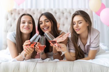 Pijama partisi. Çekici, pijamalı, gülümseyen kadınlar yatak odasında pijama partisi yaparken şampanya içiyorlar..