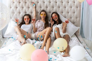Pijama partisi. Çekici, pijamalı, gülümseyen kadınlar yatak odasında pijama partisi yaparken şampanya içiyorlar..