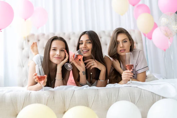 Pajamafest. Attraktiva unga leende kvinnor i pyjamas dricker champagne samtidigt som de har en pyjamasfest i sovrummet. — Stockfoto