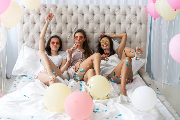 Pajamafest. Attraktiva unga leende kvinnor i pyjamas dricker champagne samtidigt som de har en pyjamasfest i sovrummet. — Stockfoto