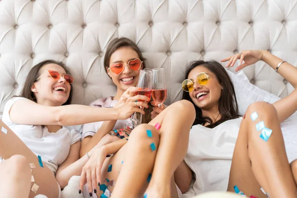 Pidżama party. Atrakcyjne młode uśmiechnięte kobiety w piżamie pijące szampana podczas piżama party w sypialni. — Zdjęcie stockowe