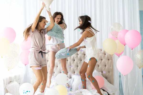 Три привлекательные девушки в пижаме улыбаются и жестикулируют, прыгая в спальню с конфетти, летающей повсюду — стоковое фото