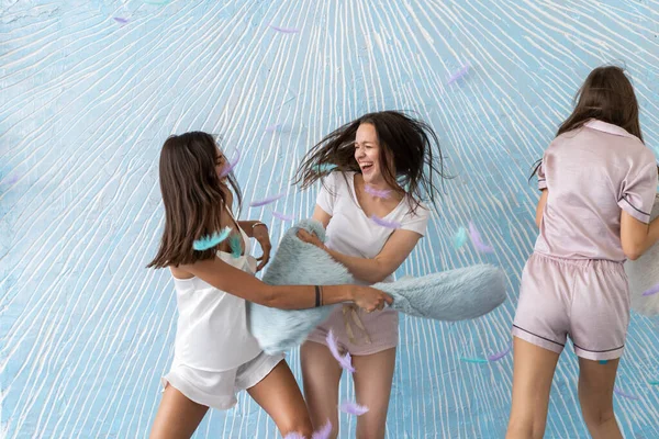 Kissenschlacht. Schöne lächelnde weibliche Models im stylischen Pyjama spielen und kämpfen mit Kopfkissen bei Pyjama-Party. — Stockfoto